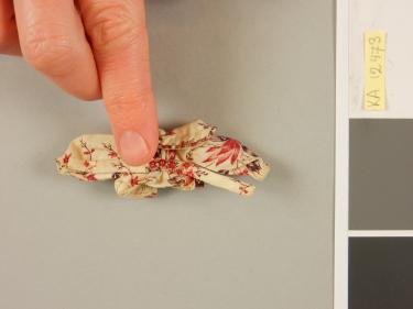 Bovenkleding in miniatuur. De vinger geeft de schaal van het kledingstuk aan. Foto: Judith van Amelsvoort.