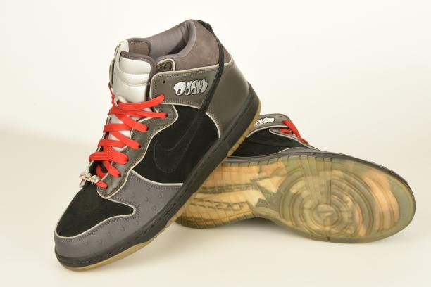 Paar zwarte en grijze enkelhoge sneakers met feloranje veters, Nike x MF Doom, Dunk High uit 2007, bruikleen Thomas van Vliet